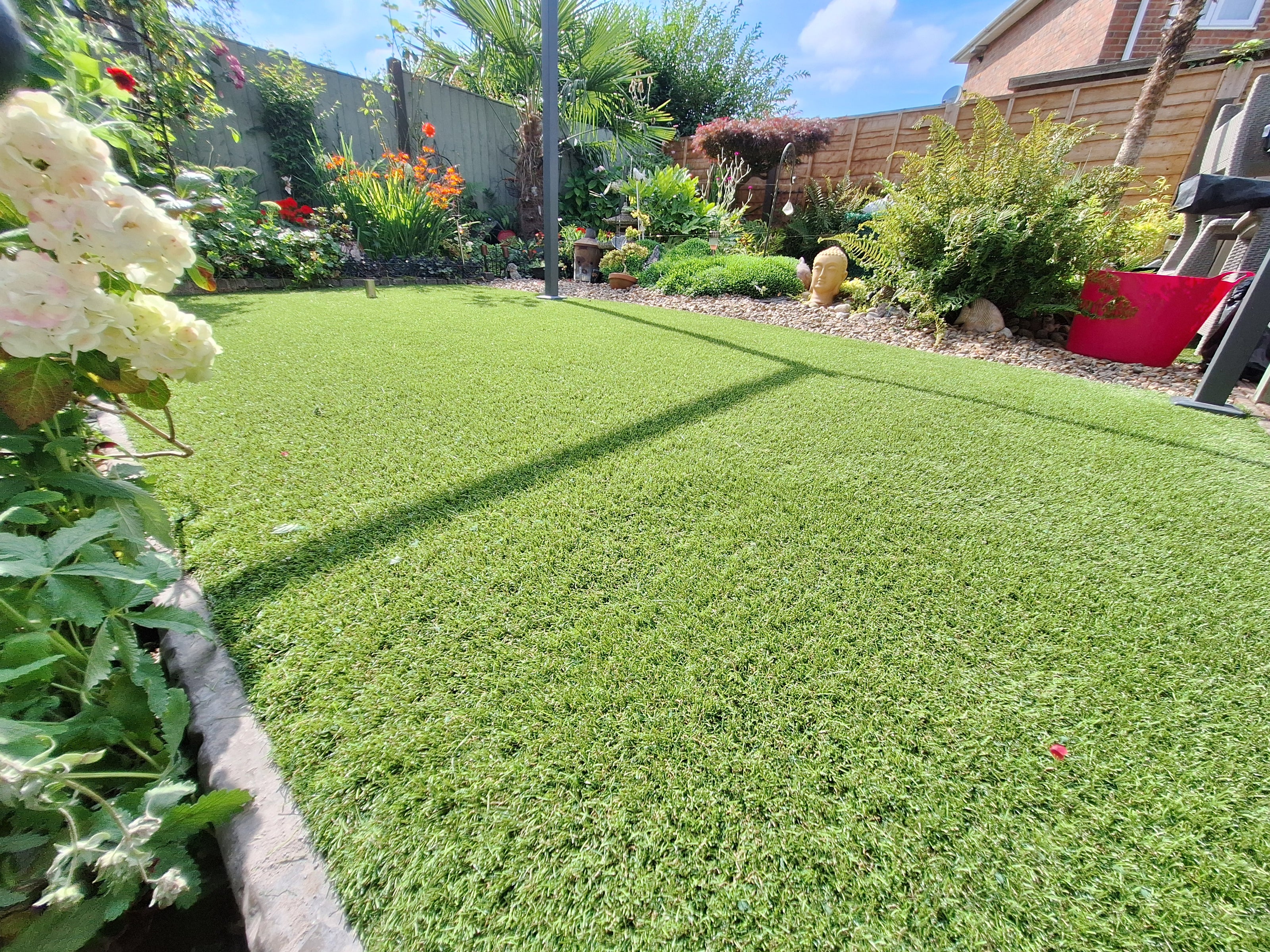 Picture shows colourful flowers and shrubbery framing an artificial grass lawn