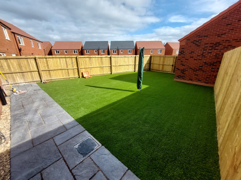 fence and houses in the background with a large artificial grass garden and patio area