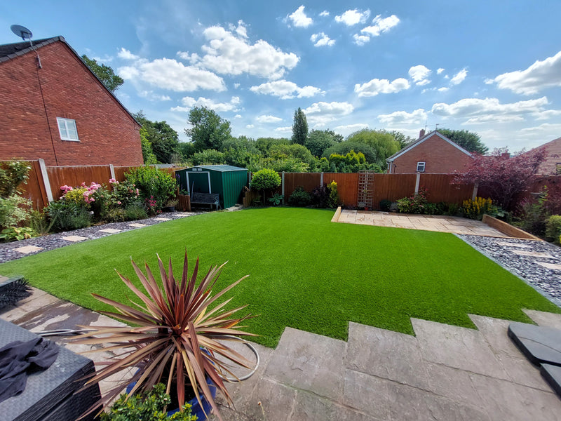 a large artificial turf lawn, blue sky, shrubs around garden perimeter
