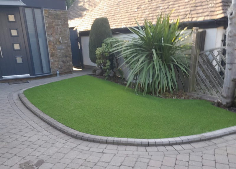 a shaped artificial lawn with palm tree in the border and front porch to the left hand side with grey door